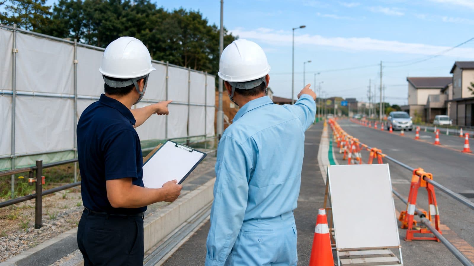 道路工事の規制帯を前に現場担当者と打ち合わせをする営業担当のイメージ
