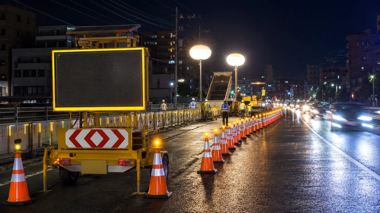 ソーラー式電光標示板とバルーン照明、保安灯付きコーンで規制した夜間の道路工事現場のイメージ
